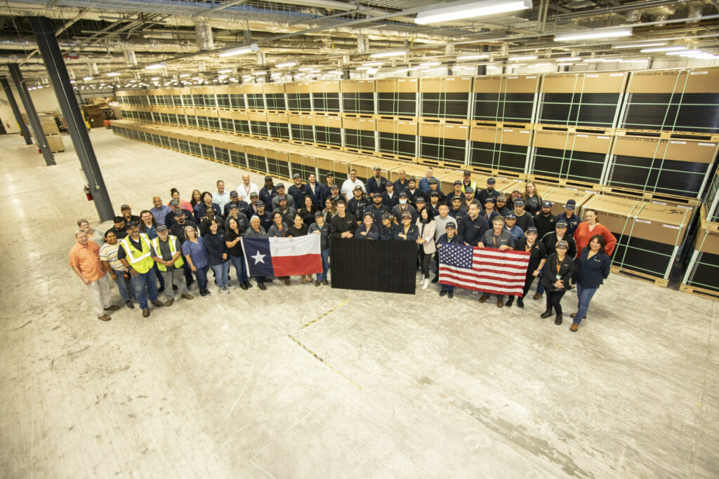 Mission Solar team proudly posing with American flag, Texas flag, and solar panel at company facility, representing USA-made solar energy and Texas manufacturing.