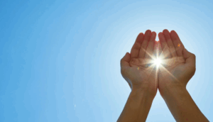 Hands cupping sunlight against blue sky.