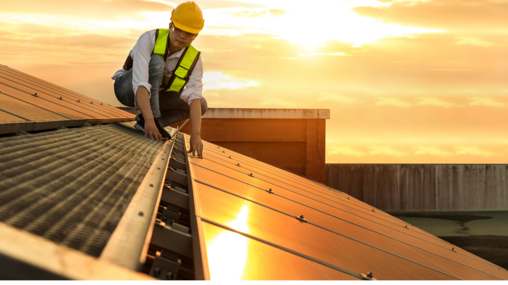 Worker installing solar panels on rooftop at sunset
